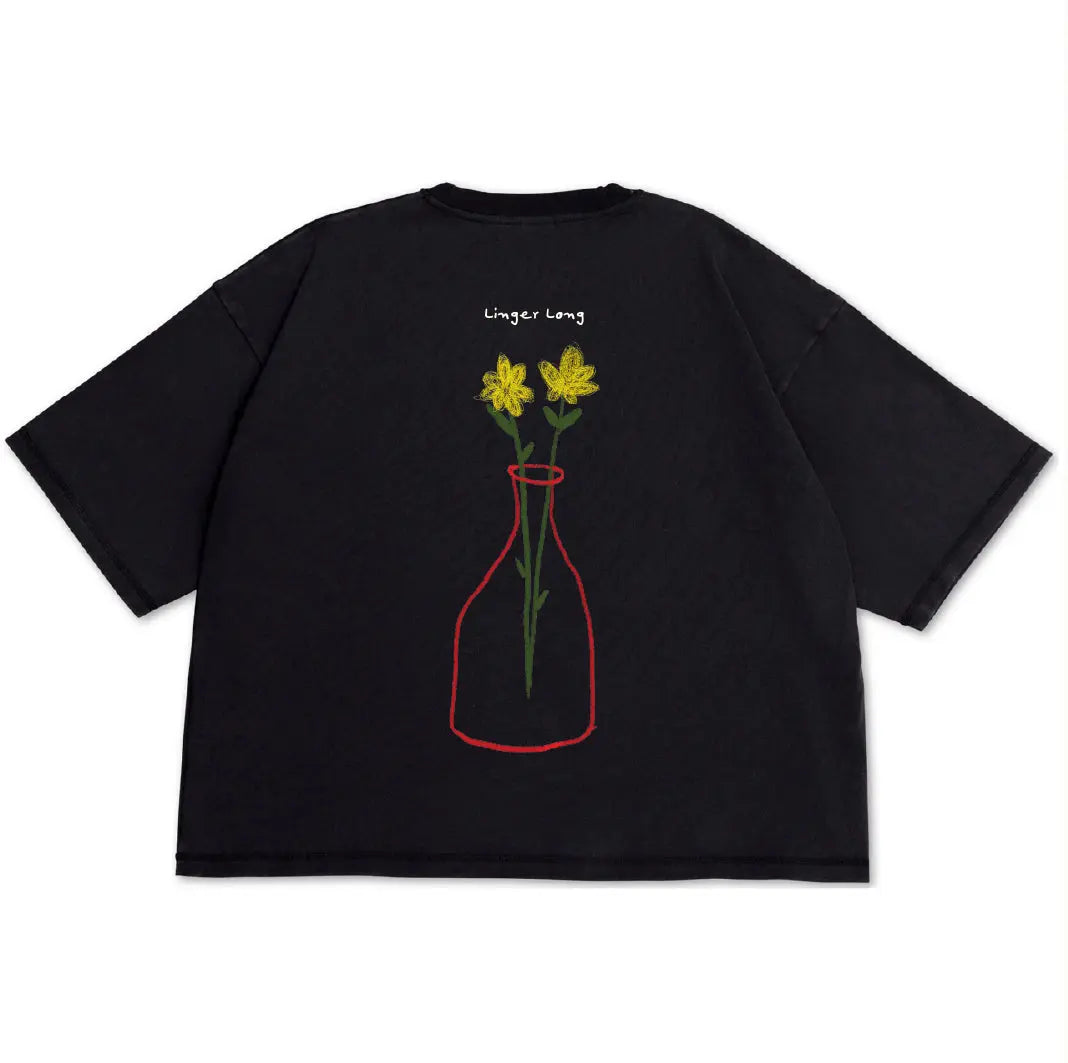 A black short-sleeve t-shirt with a graphic of yellow flowers in a red-outlined vase on the front, with the text 'Linger Long' printed above. The shirt is displayed flat against a solid white background.