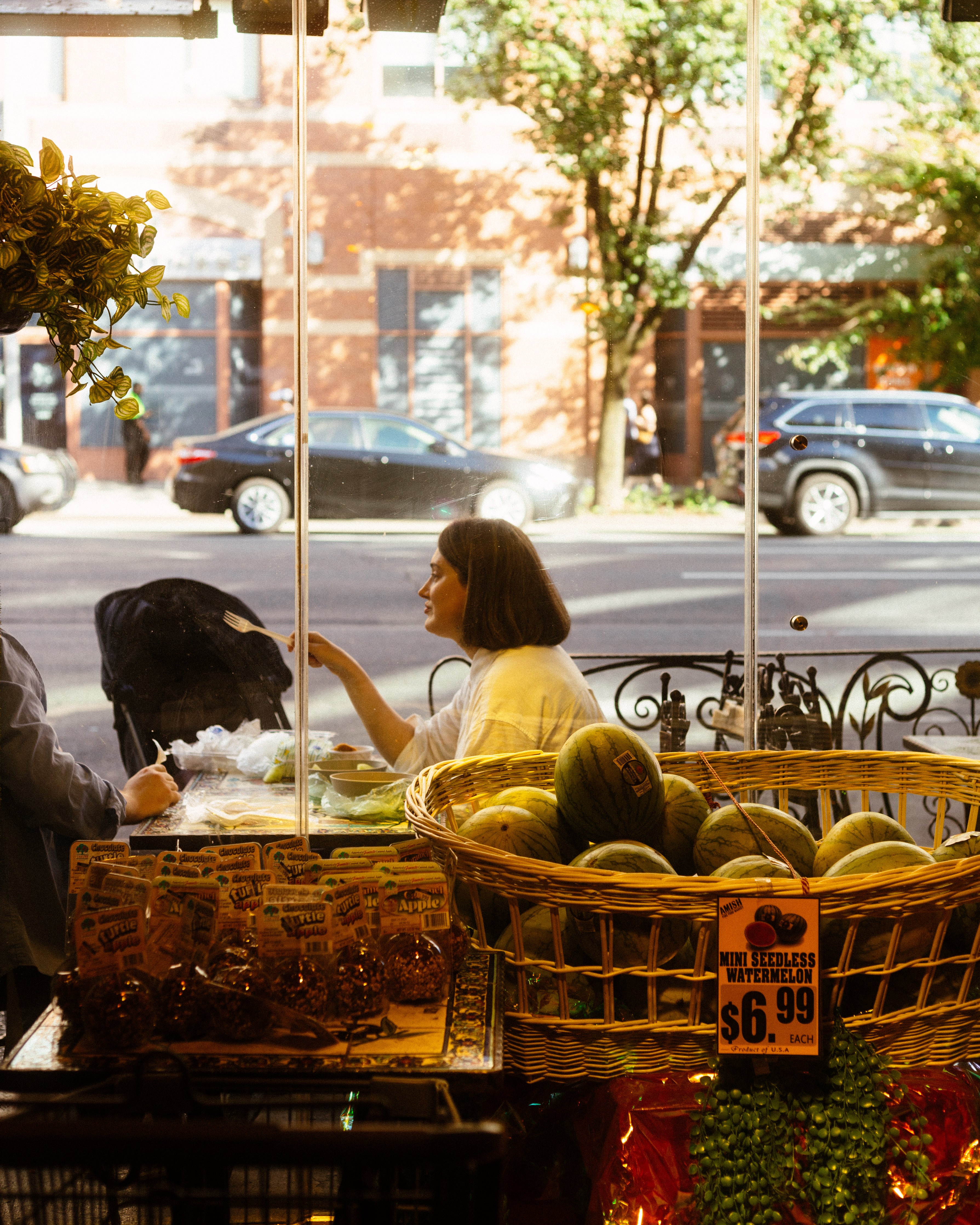 lady seating outside in a table eating food and talking. Inside theres mini seeless watermelon for 6.99.