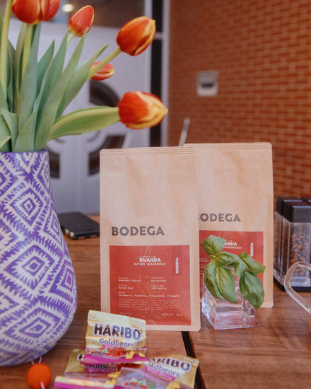 Bodega coffee bags and Haribo candy on a table with tulips in the background